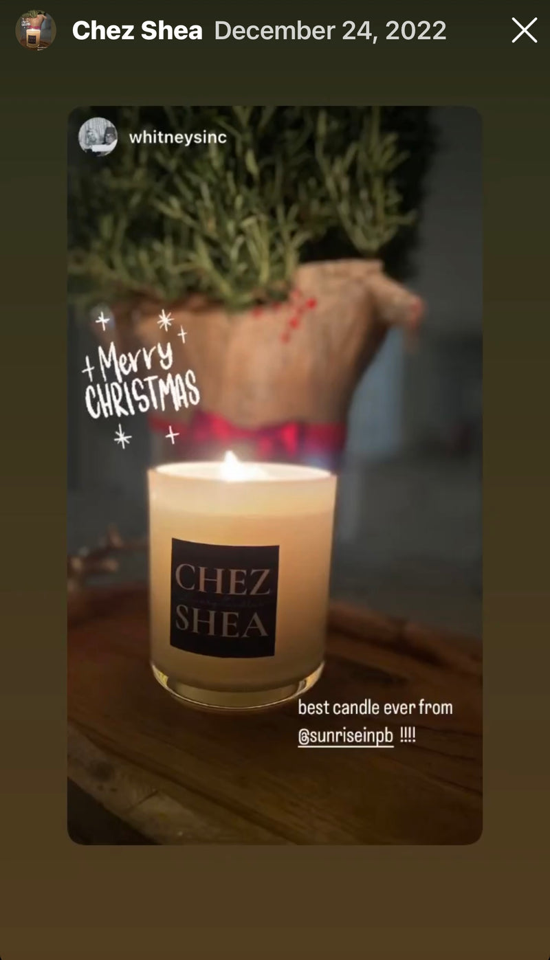 Candle with 'Chez Shea' label and Christmas decoration in the background